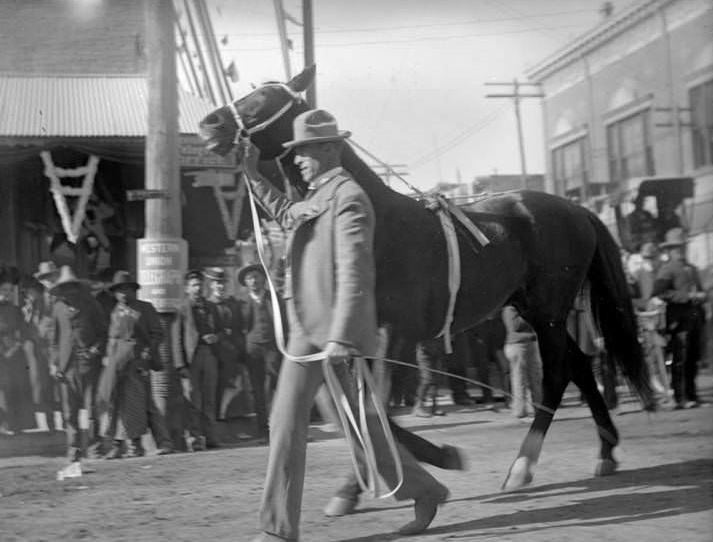 Man walking horse, parade, 1907