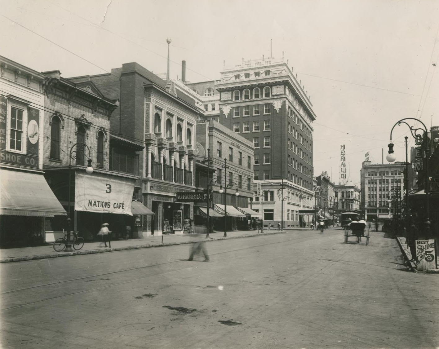 A street in El Paso with various stores seen on the side to the left and a sign for the "Herald" seen in the background, 1900s