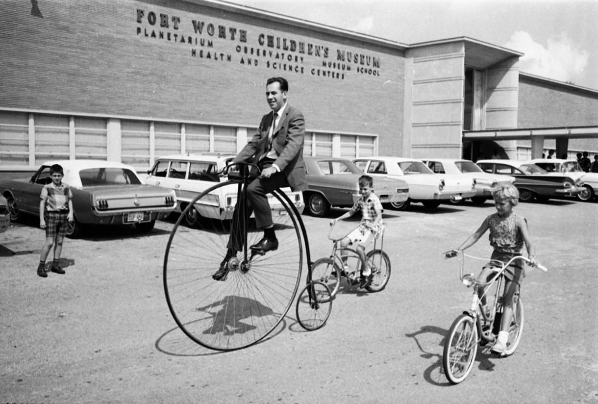 Helmuth Naumer, director of Fort Worth Children's Museum, rides an old fashioned bicycle, 1967