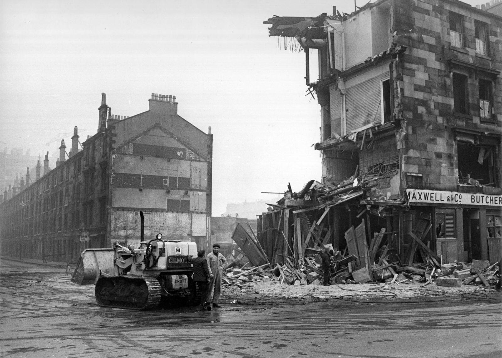 Workmen and a bulldozer beside a tenement being demolished in the Gorbals area of Glasgow, 1960
