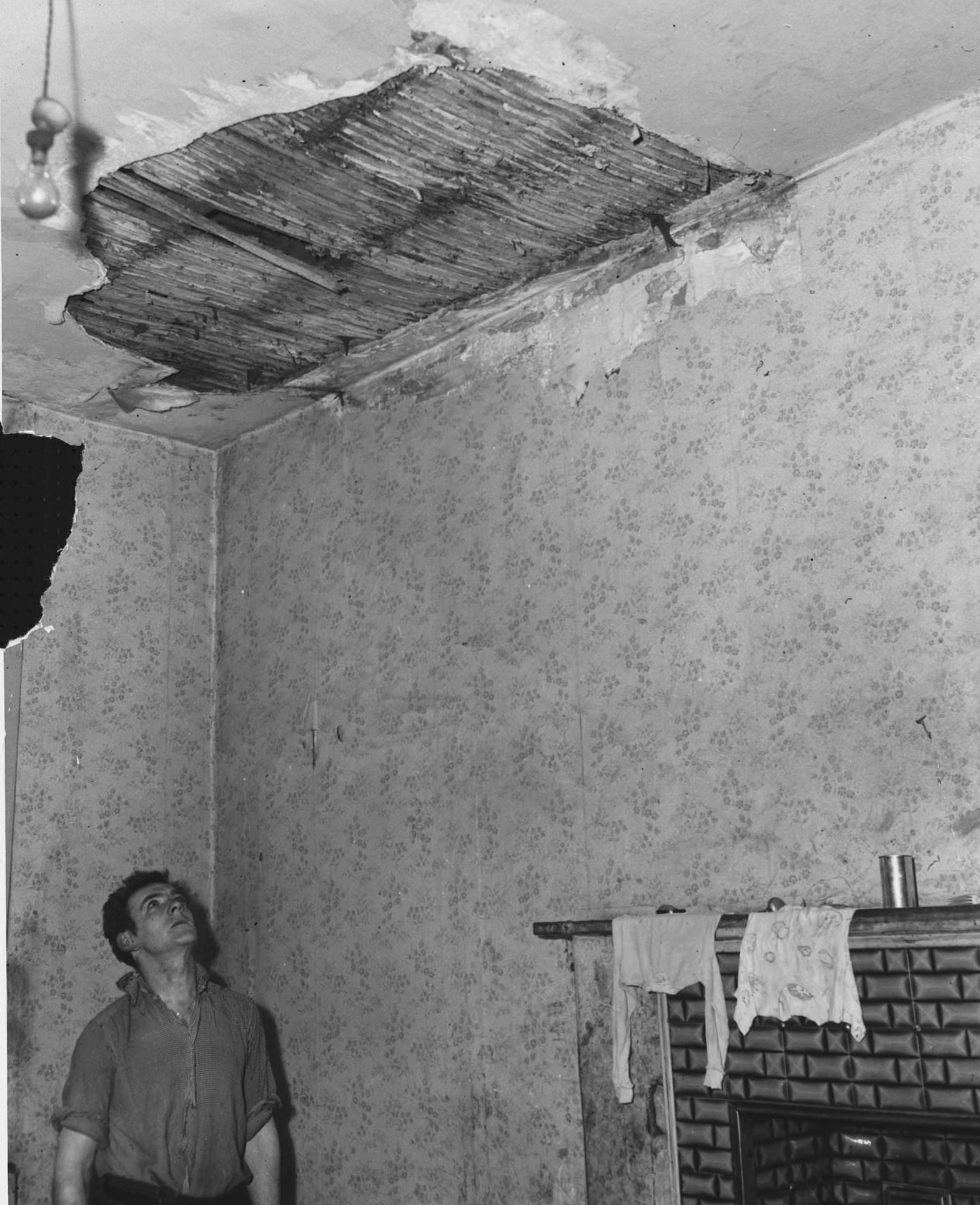 Mr. Jackson inspects a hole in the ceiling of his council house in the Gorbals, 1956