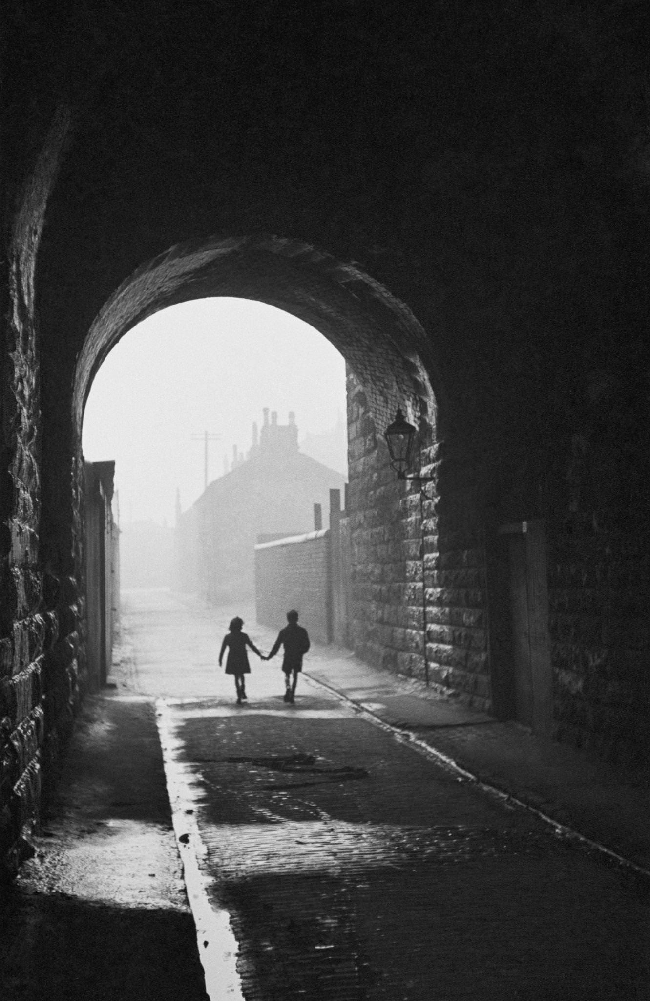 A boy and girl hold hands under an archway in the Gorbals, a slum district of Glasgow, 31st January 1948.