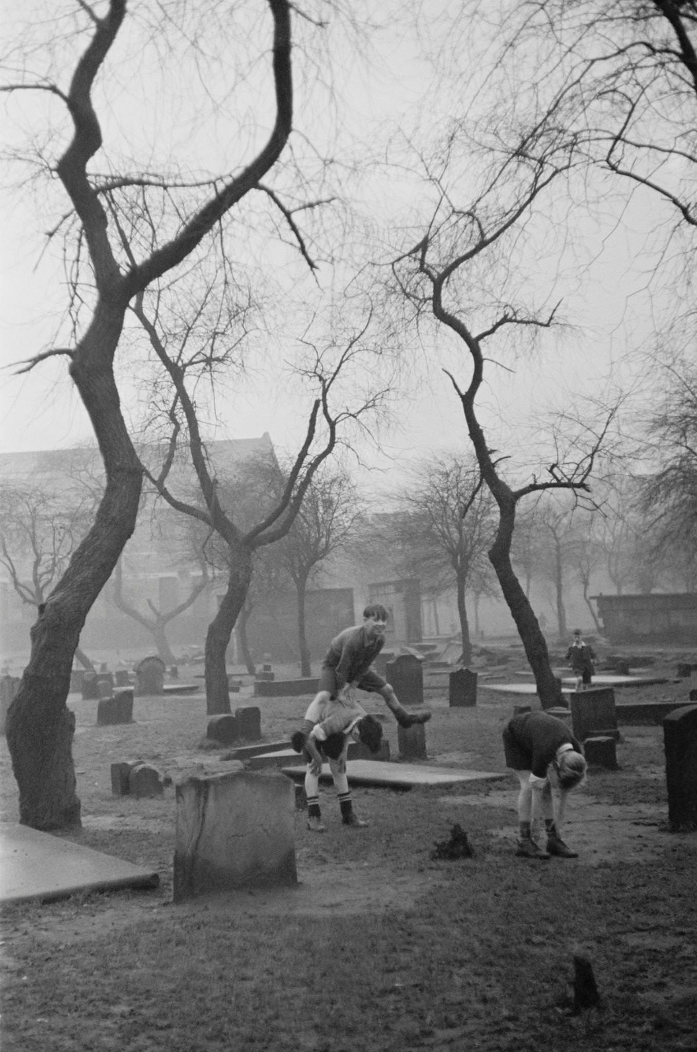 A group of boys playing leapfrog amongst the gravestones of the Corporation Burial Ground in Rutherglen Road, one of the few areas of greenery in the Gorbals, a slum district of Glasgow, 1948.