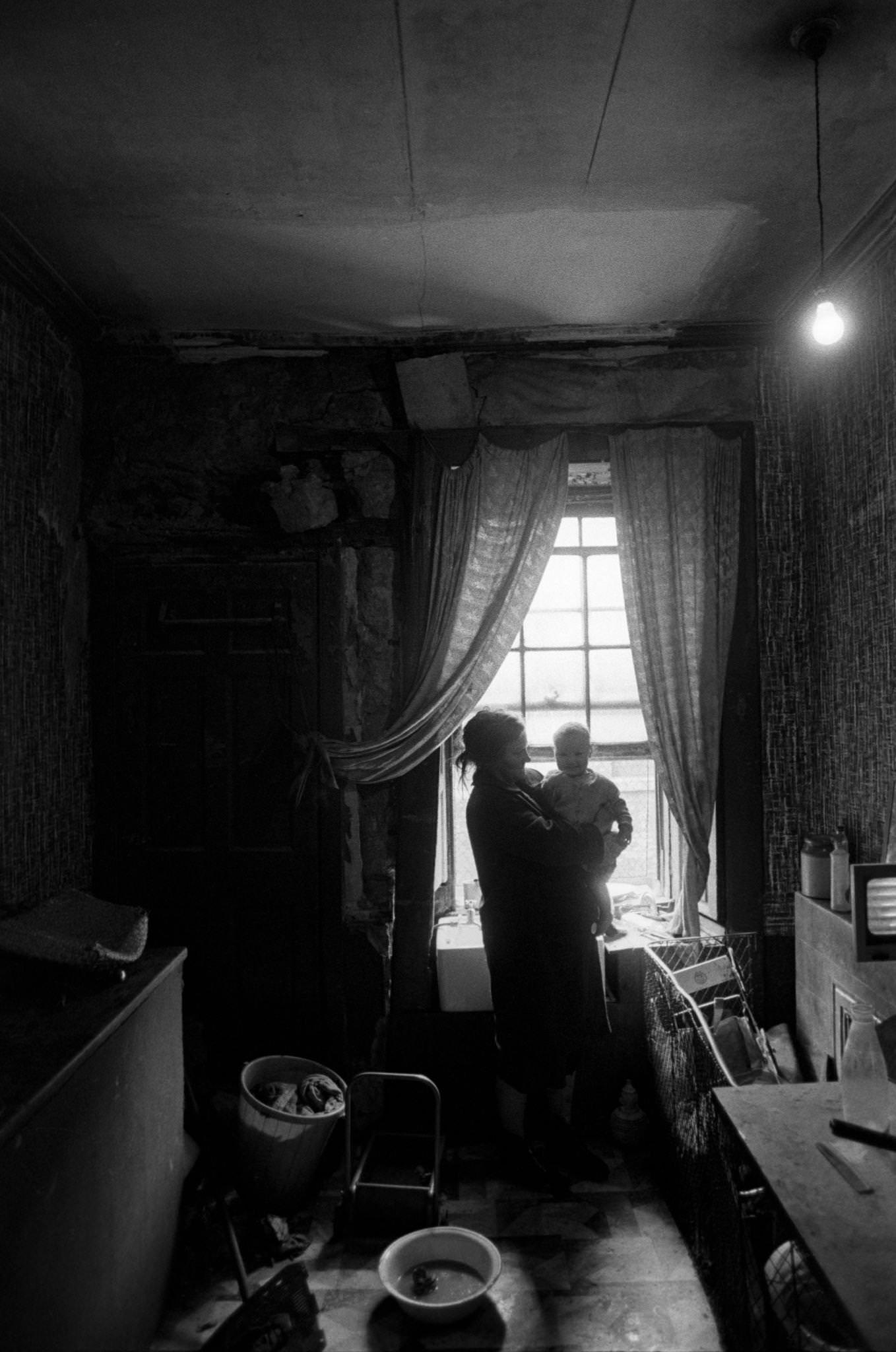 A mother holding her child at a window in the kitchen of her flat in the notorious Gorbals district of Glasgow, 1969.