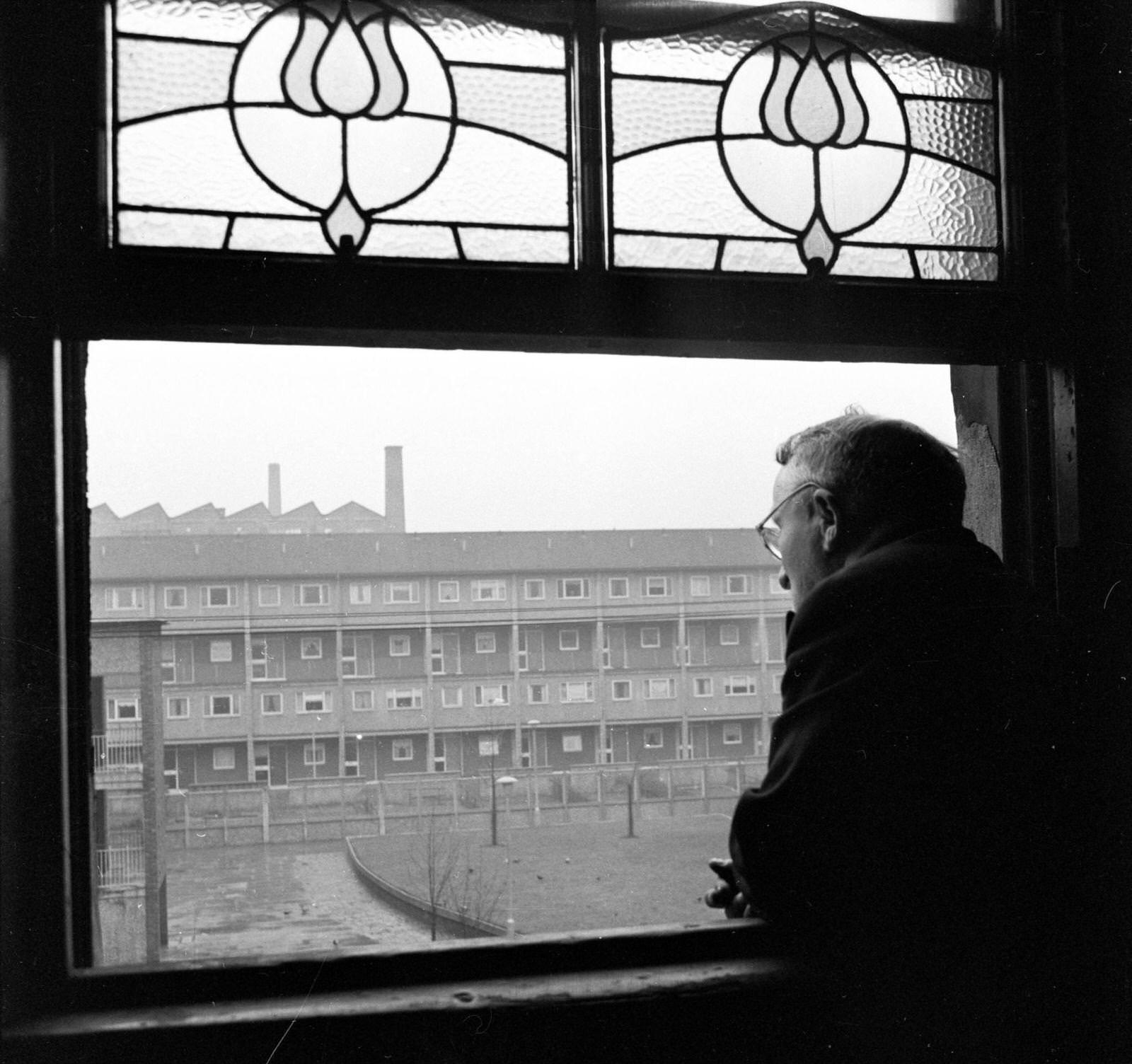 A resident of the Gorbals area of Glasgow looking out of his window at a row of newly-built housing, 1962