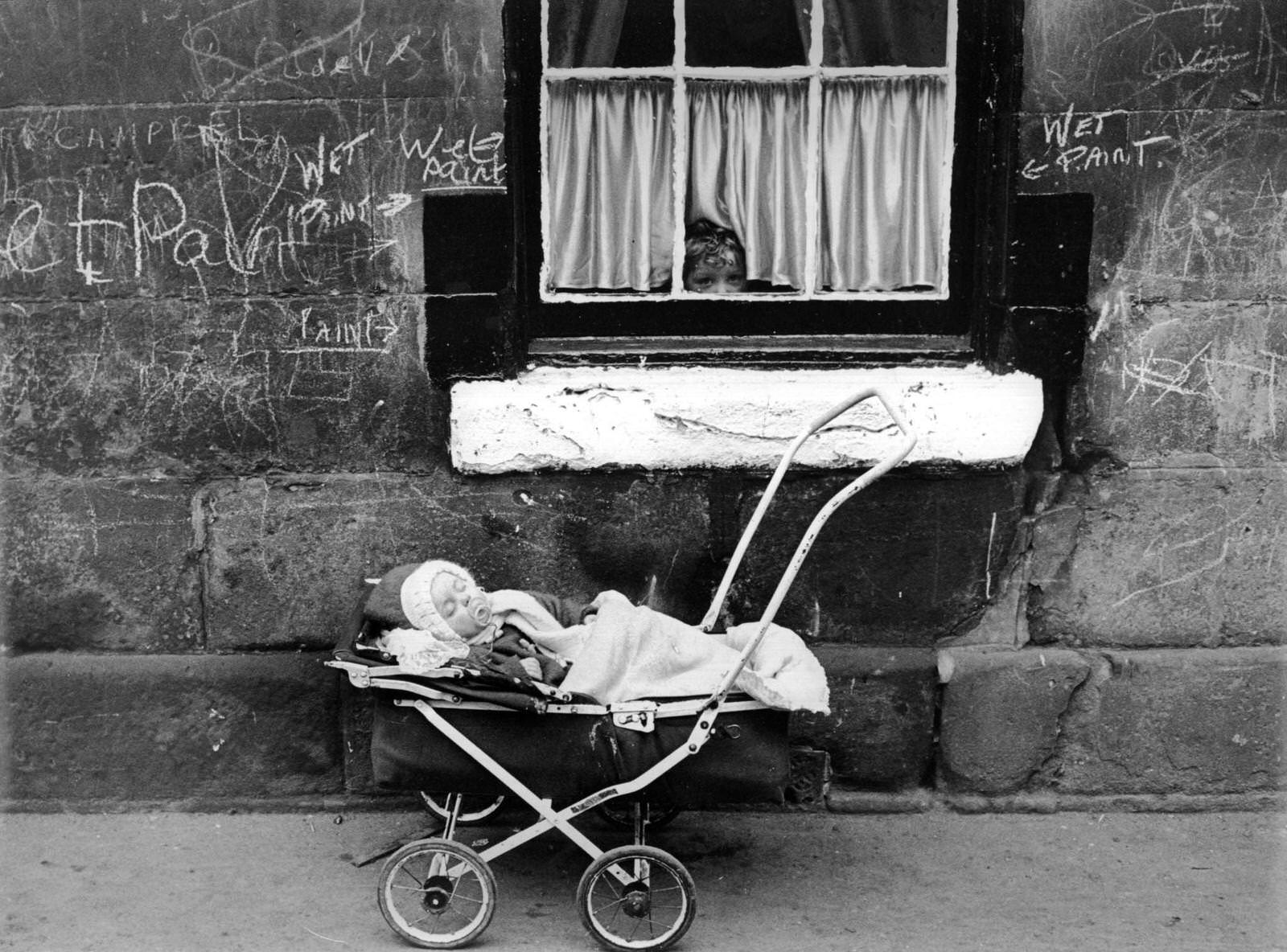 A child looks at a baby in a pram from the window of a tenement block in the Gorbals area of Glasgow, before demolition, 1960