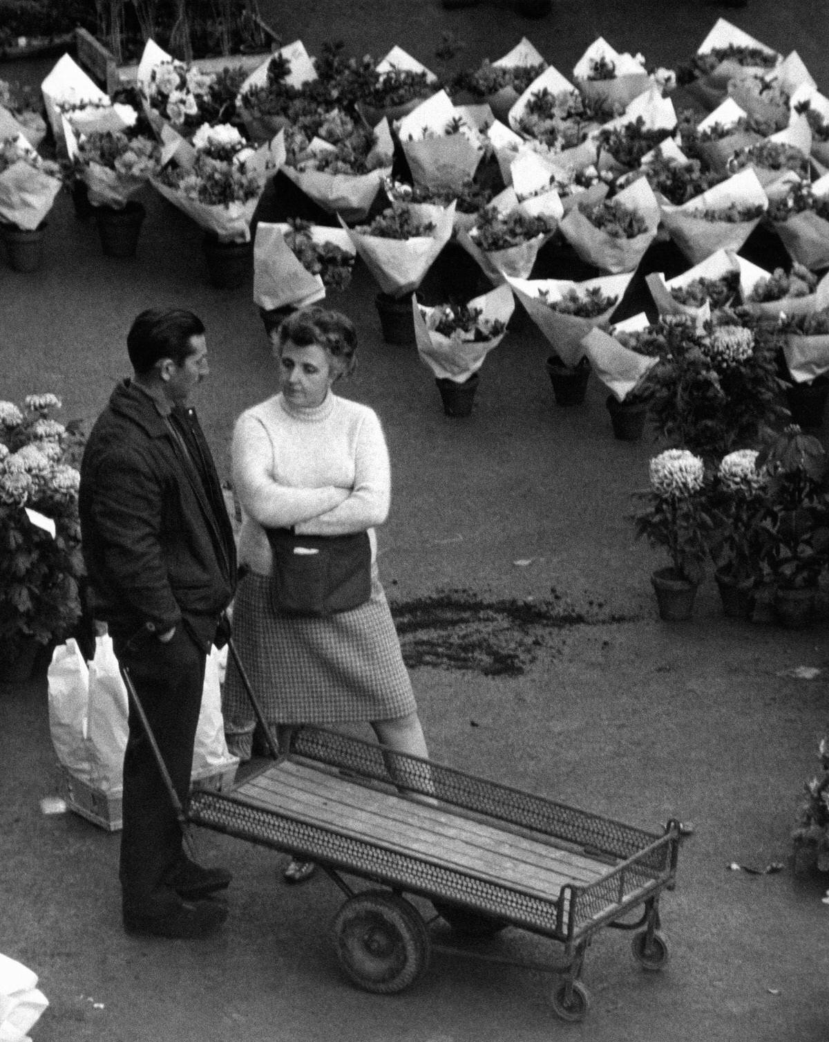 A woman and a man speaking surrounded by bunches of flowers in Les Halles, 1967