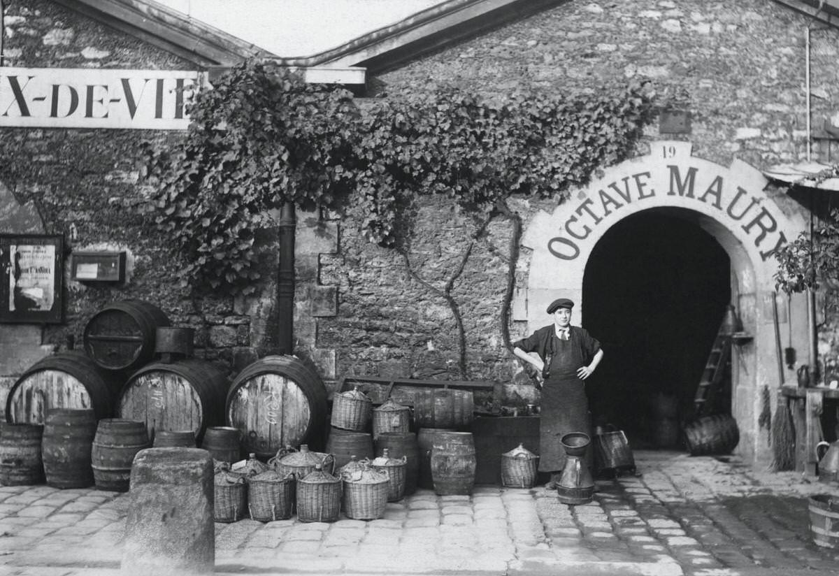 A worker standing with barrels and baskets outside the entrance to Octave Maury at the wine sellers storehouse in Les Halles, 1920s