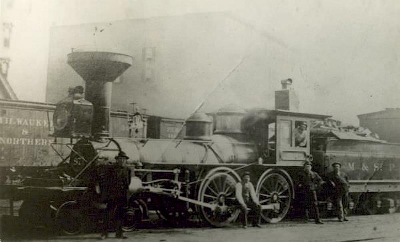 Several men pose with the Chicago, Milwaukee & St. Paul Railway engine #87, built by Schenectady Locomotive Works, 1885. This image was taken near Cherry Street.