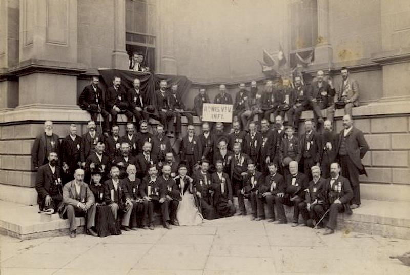 Group portrait of the members of the 11th Wisconsin Volunteers, and some family members, posed on the steps of what appears to be the old Milwaukee County Court House during a reunion, 1895