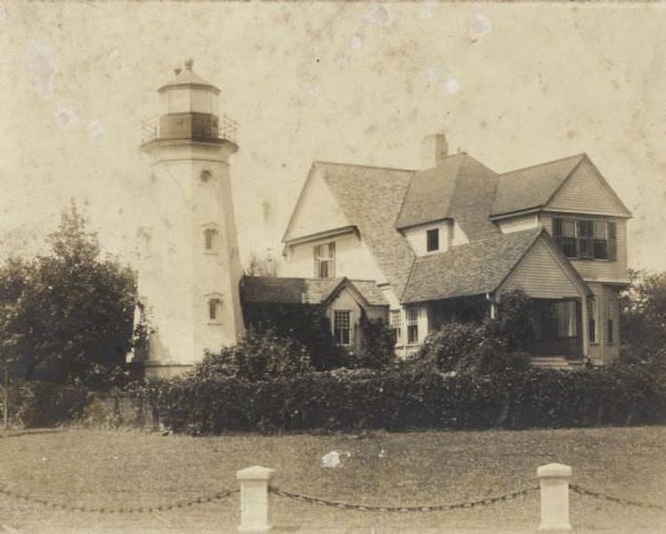 A chain and posts border the yard of the lighthouse, which is attached to a two-story house, 1895