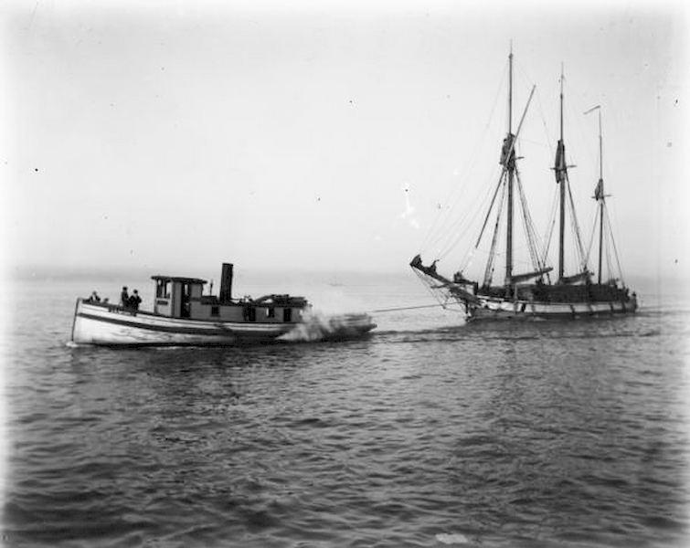 View across water of a tugboat pulling a sailboat towards Milwaukee on Lake Michigan, 1898