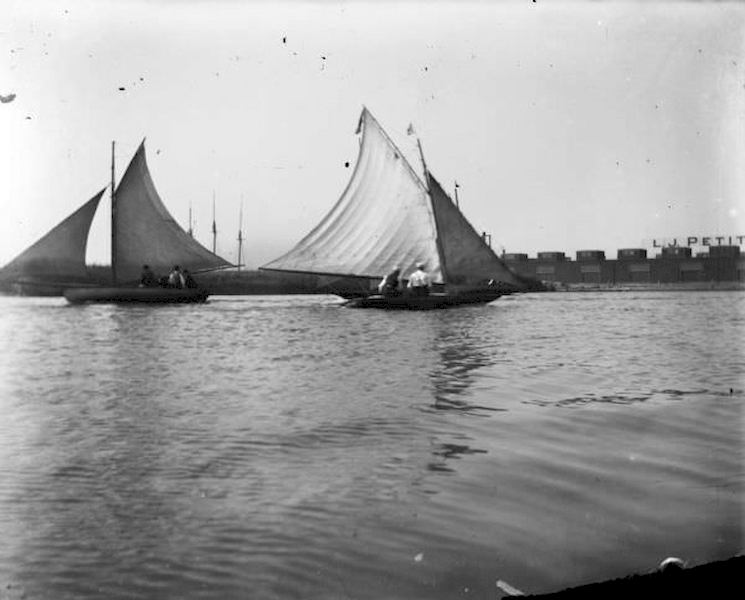 Small sailboats in Milwaukee Harbor with buildings on the far shoreline in the background, 1898