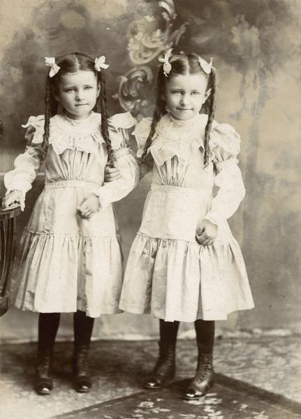 Twins Emma (1893-1974) and Marge (1893-1973) Willms of Milwaukee, Wisconsin standing in front of a painted backdrop, 1898
