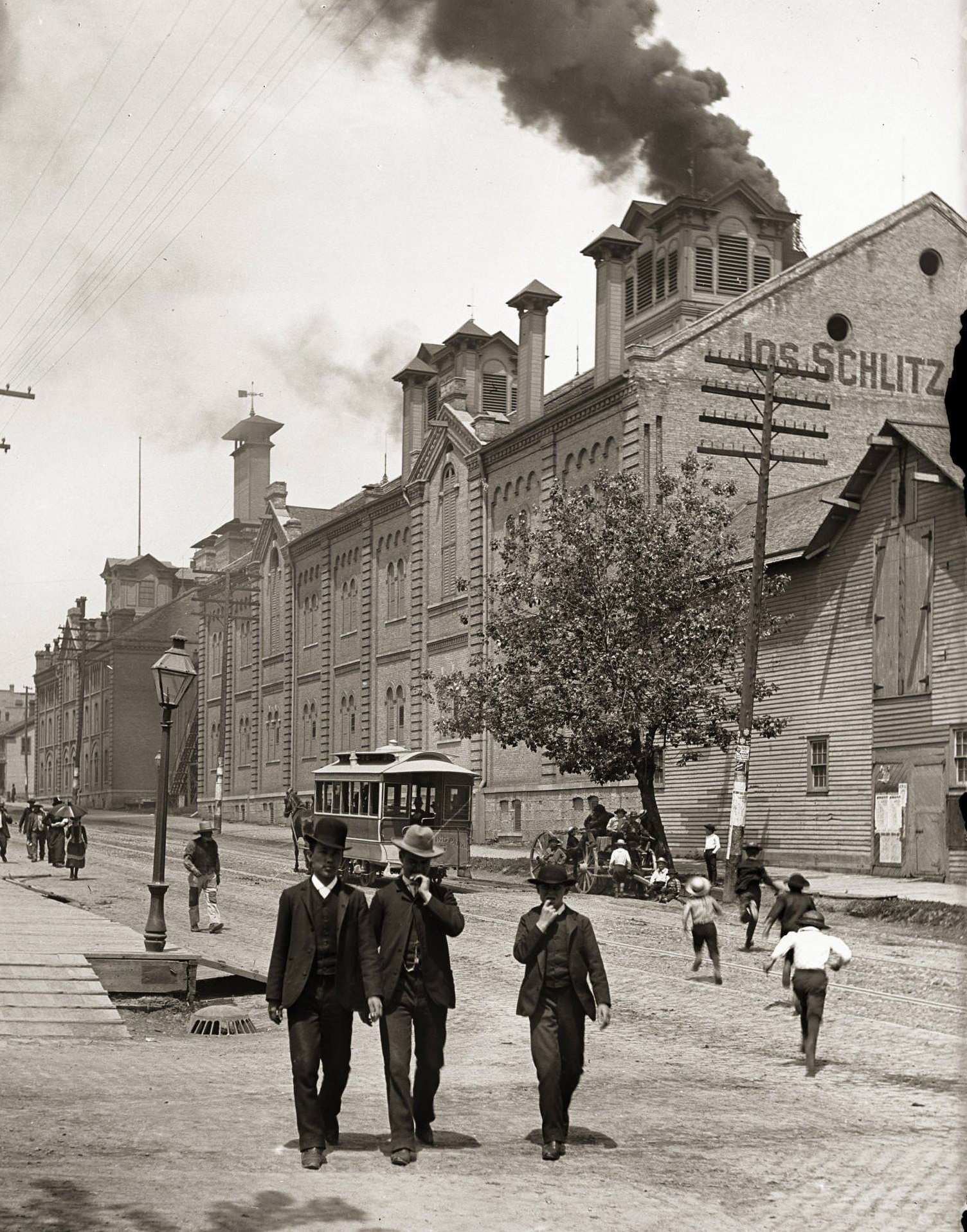 Exterior of Schlitz Brewing Company with two men and a boy in suits and hats in the foreground, Milwaukee, Wisconsin, 1888.