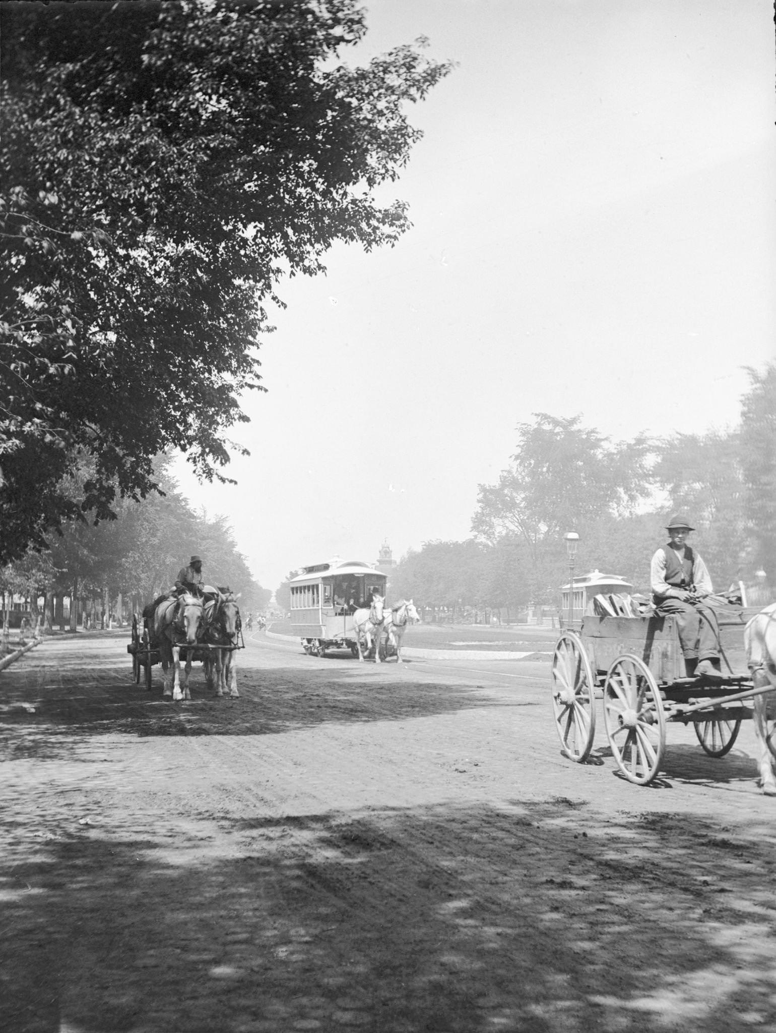 View looking up Grand Avenue from 9th Street toward two horse-drawn wagons and a horse-drawn streetcar on tree-lined street, Milwaukee, Wisconsin, 1885.