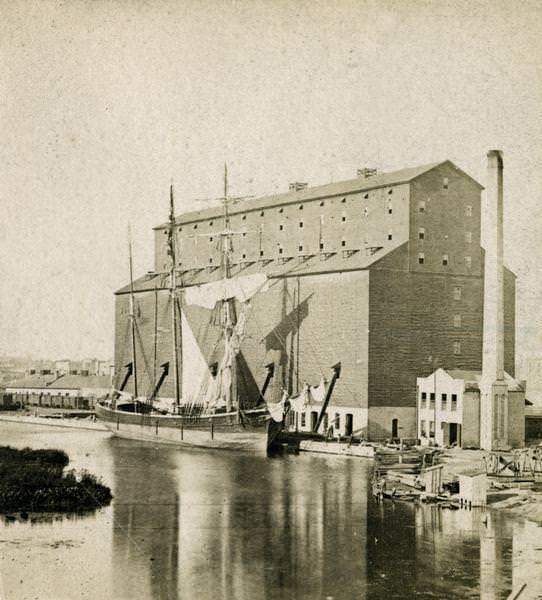 The Milwaukee & St. Paul Railway Company grain elevator at the Milwaukee harbor, with a sailing ship anchored nearby, 1870