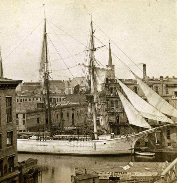 Elevated view of Milwaukee River with large sailing ship - a two-masted schooner - entering the port, 1870