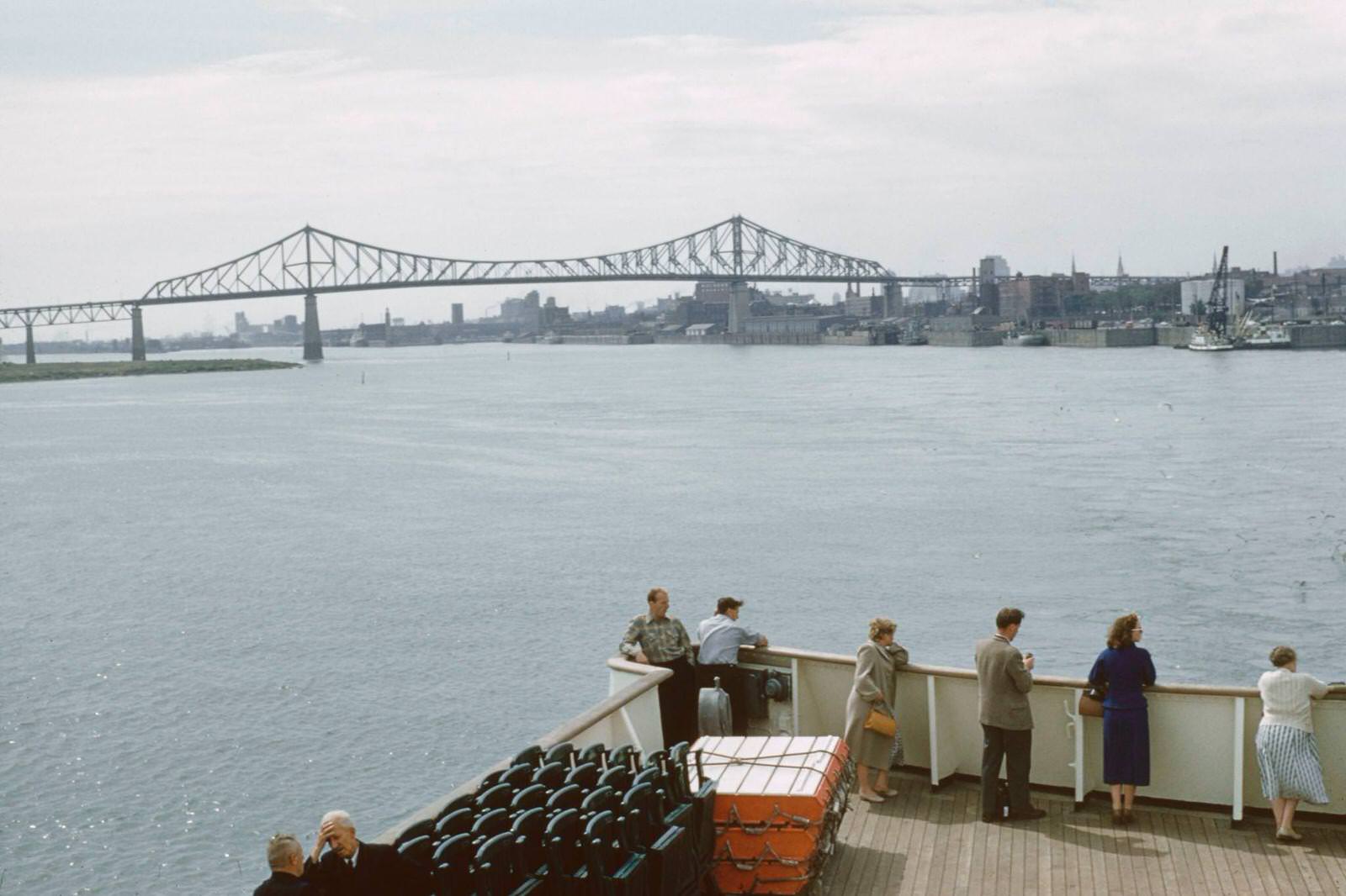 Passengers stand on the deck of a boat on the St Lawrence River beside the port district of the city of Montreal in the province of Quebec in Canada, 1960.