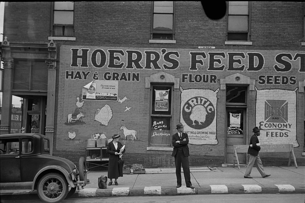 Waiting for a bus in front of feed store, Peoria, Illinois, 1938