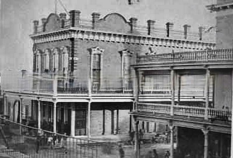 Crowd gathers on sidewalk and balcony of brick building at corner of 10th and K Sts, 1880