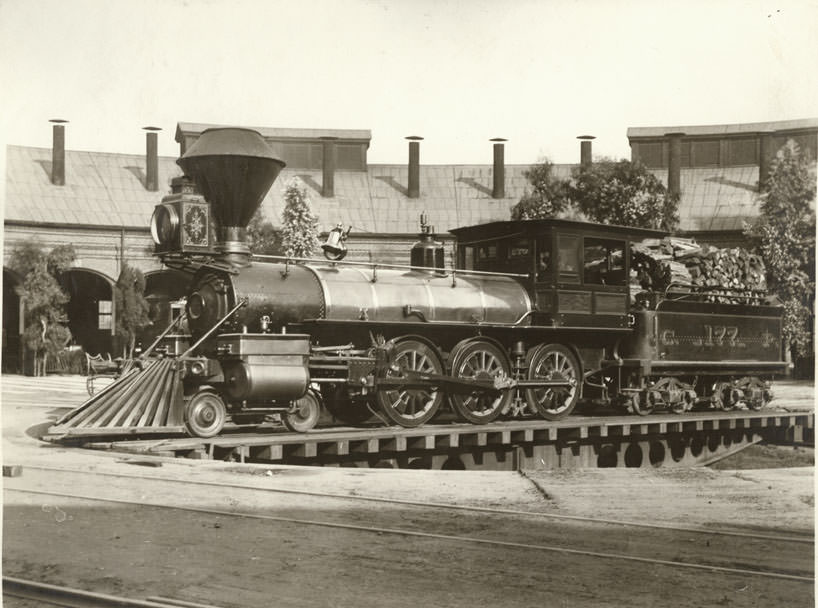 View of locomotive, no. 177 and tender, on turnabout at roundhouse; roundhouse in background. Built at Sacramento in 1886.