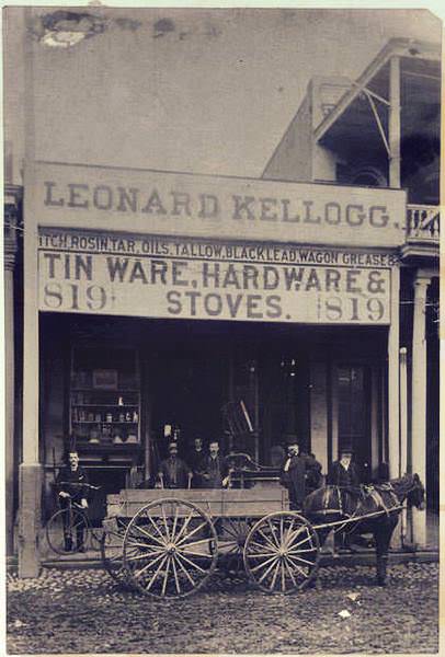 View of a horse-drawn wagon in front of Kellogg's store. Six men posed in front of the store, man on the left next to a bicycle, 1880