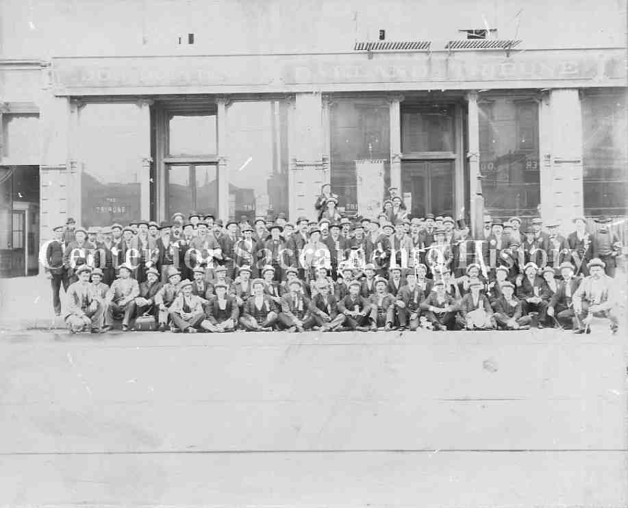 acramento butchers gathered in front of Oakland Tribune building, posing with a banner, probably as part of a convention or meeting, 1885