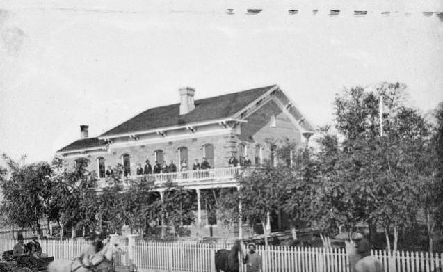 Home of W. H. Williams with a group of people posing outside on the balcony.W. H. Williams Home 1887.