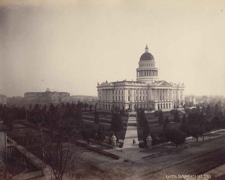 Angle view of the capitol building in sacramento, railroad tracks are seen in the foreground, and the rest of the city is seen spread out beyond, 1880