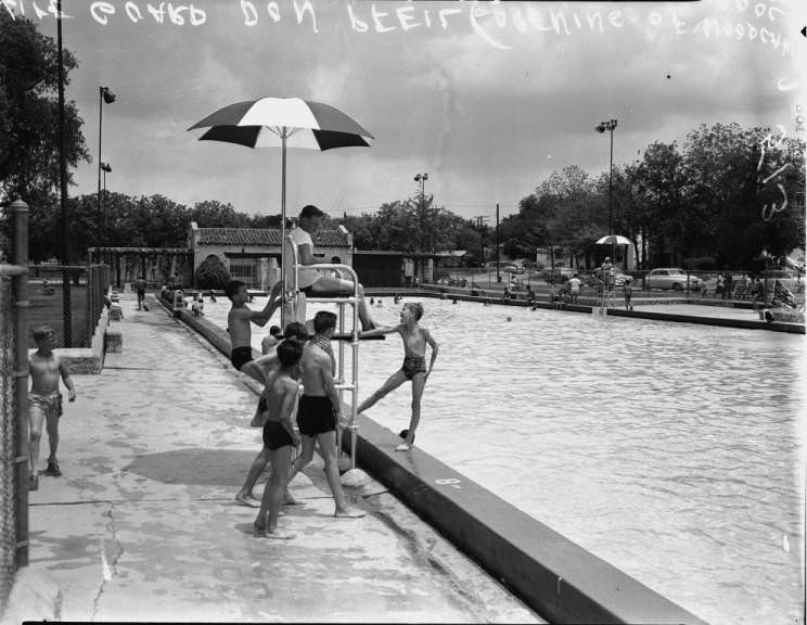 Life Guard Don Pfeil sitting in how tower while being surrounded by children at Woodlawn Pool, 1954