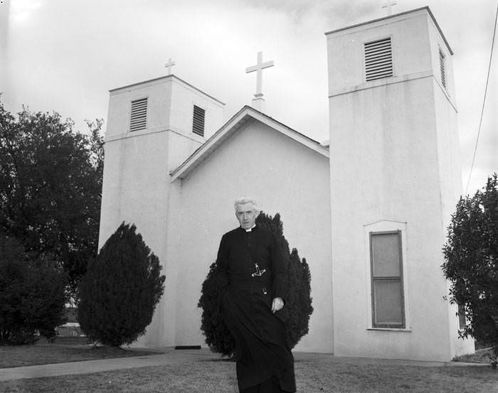 Oblate priest in front of church, 1950s