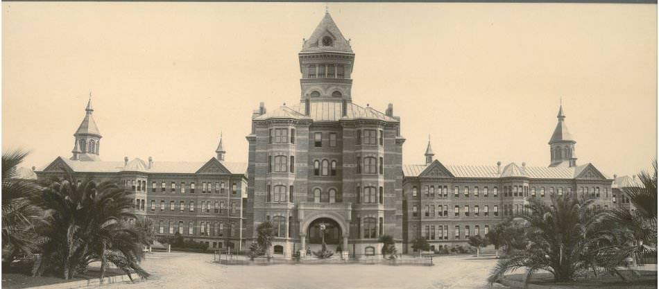 Front of Agnews State Hospital pre-1906 earthquake, showing full extent of building. Palm trees flank the left and right side of the driveway.