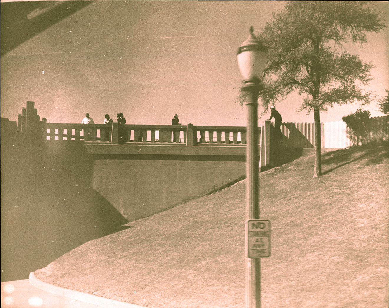 People standing on bridge overlooking grassy knoll, 1963