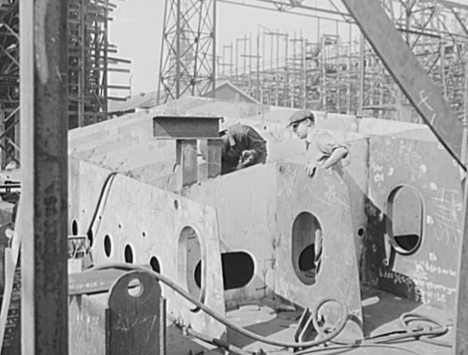 These two workers are assembling the hull section of a new cruiser. Four new navy cruisers are on the ways here, and a huge battleship, 1941
