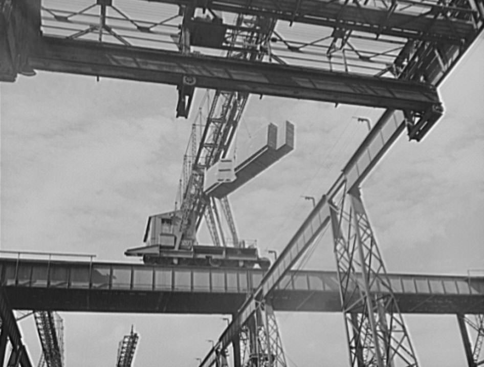 A section for a new U.S. Navy cruiser is being delivered by overhead crane to the building ways, 1941