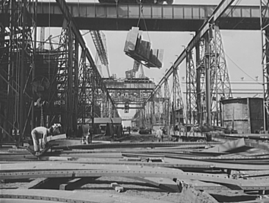 A section for a new U.S. Navy cruiser is being delivered by overhead crane to the building ways, 1941