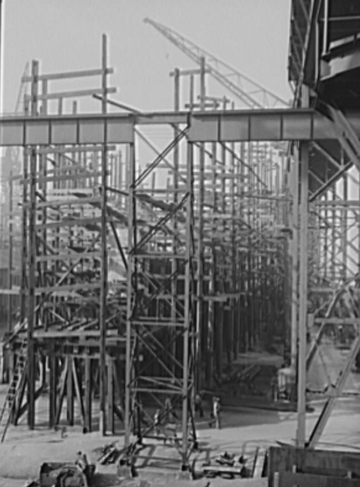 Behind all the scaffolding a new cruiser is beginning to take shape, one of four under construction on the Newport News ways, 1941
