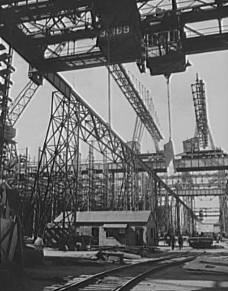 Thousands of tons of lumber and steel are used in the construction of these ways, where American mechanical genius is employed in the production of ships for our new two-ocean Navy, 1941