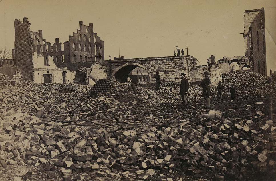 Two soldiers, three boys and piles of cannonballs among ruins, 1865