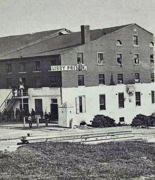 A group of people including soldiers standing outside Libby Prison in Richmond, Virginia, 1869