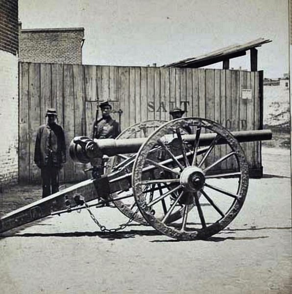 Cannon with two soldiers and a civilian awaiting shipment on a wharf in Richmond, Virginia, 1865