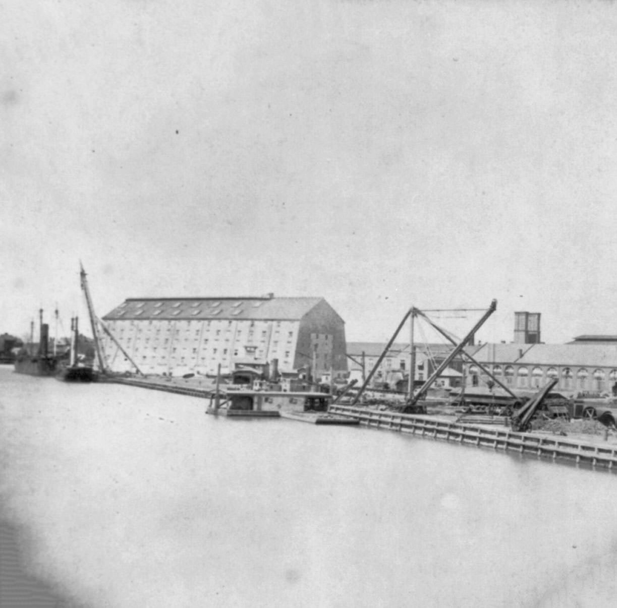 Washington Navy Yard. View of dock with large buildings and large cranes and derricks, 1867