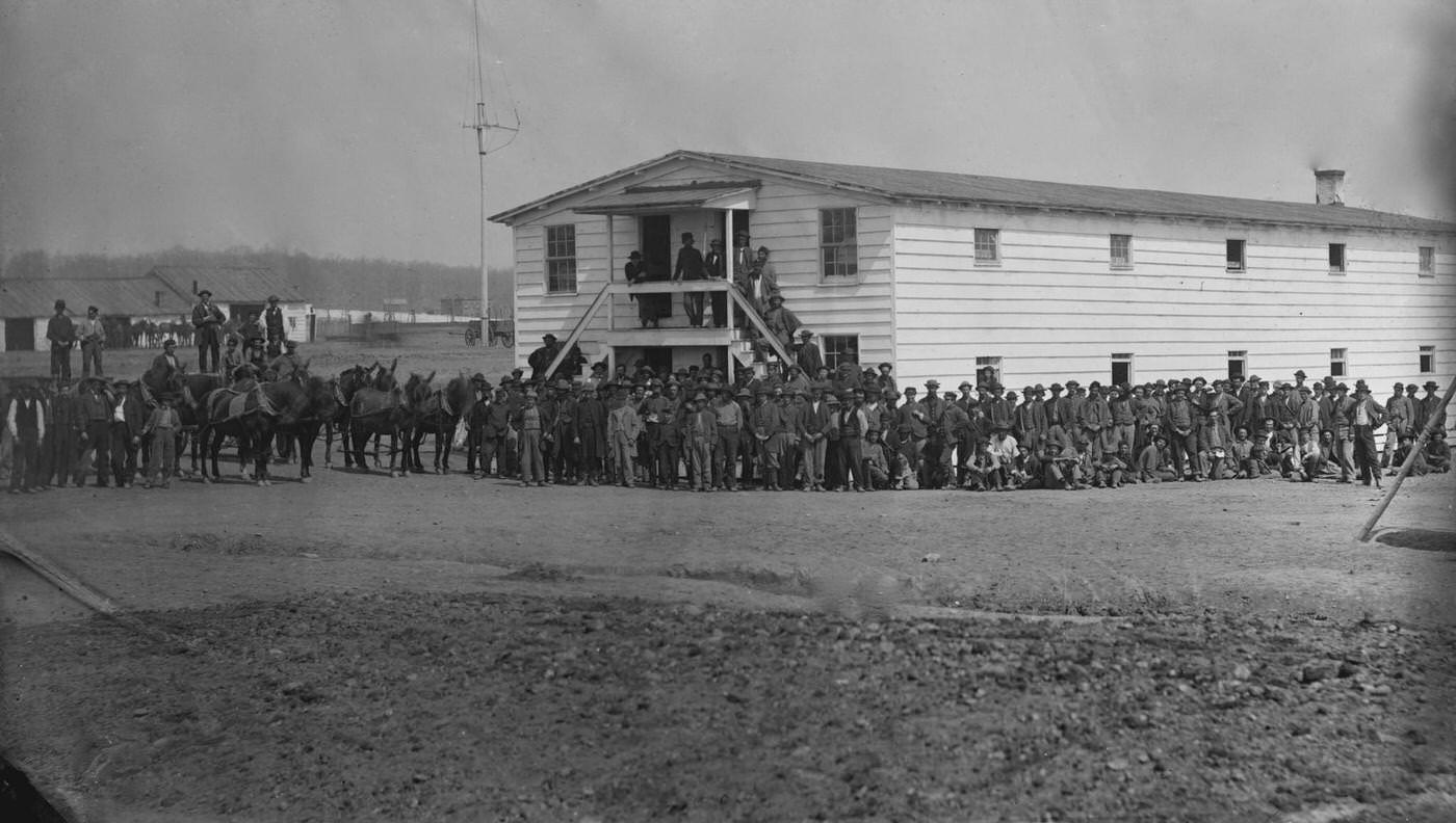 Exterior view of the mess house at the government stables, with a large group of men gathered around, Washington, D.C., 1865