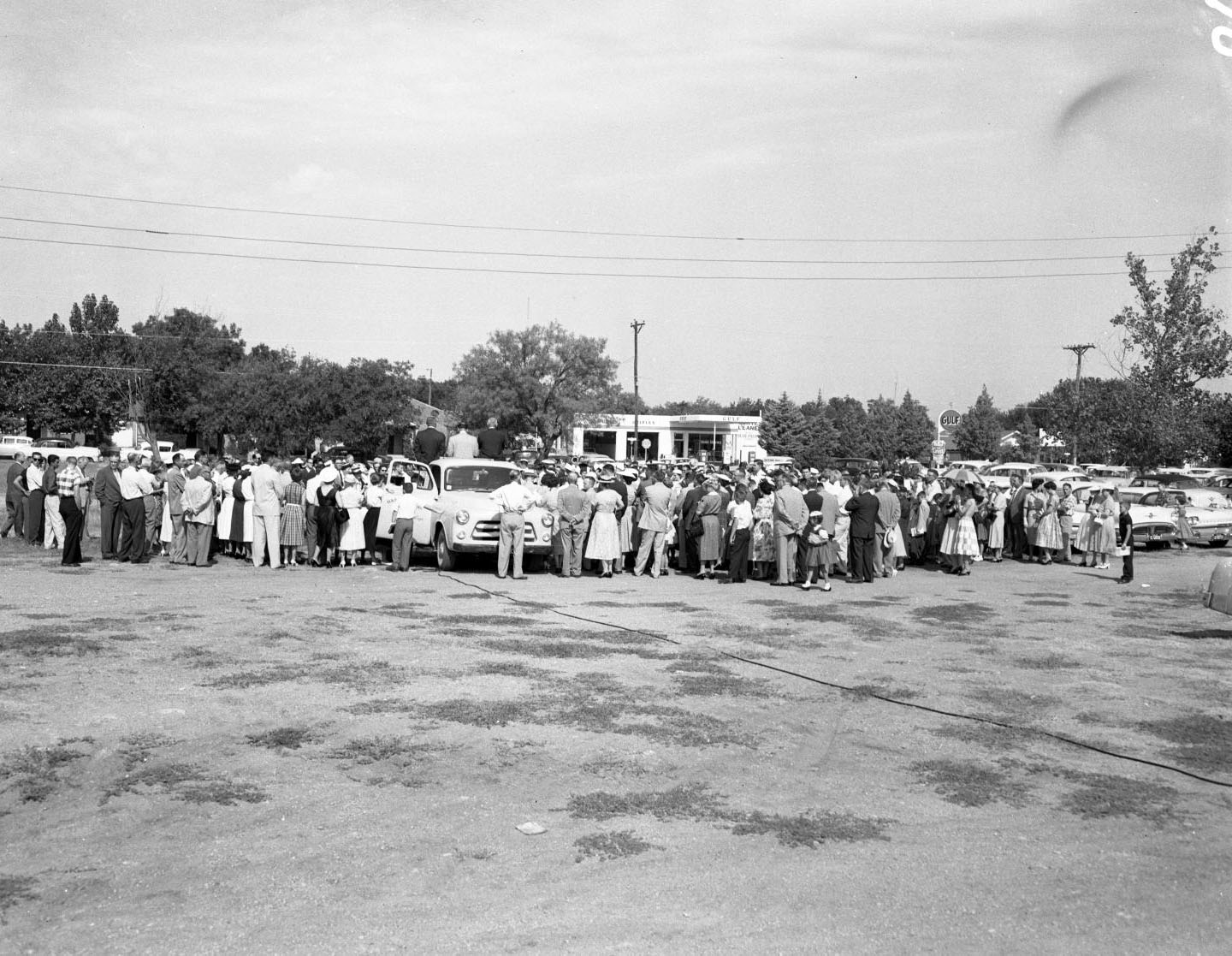 The groundbreaking of University Baptist Church, 1958. There is a crowd of people facing away from the camera. Three people are sitting on top of a truck.
