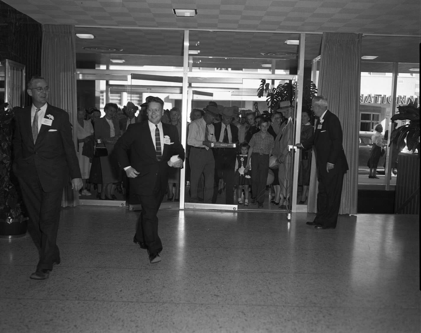 A large group of people behind the two sets of glass double doors inside of the Citizens National Bank, 1956