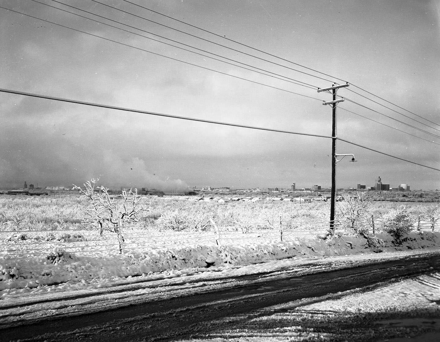 A snow covered field, road, barbed wire fence, and power lines, 1959