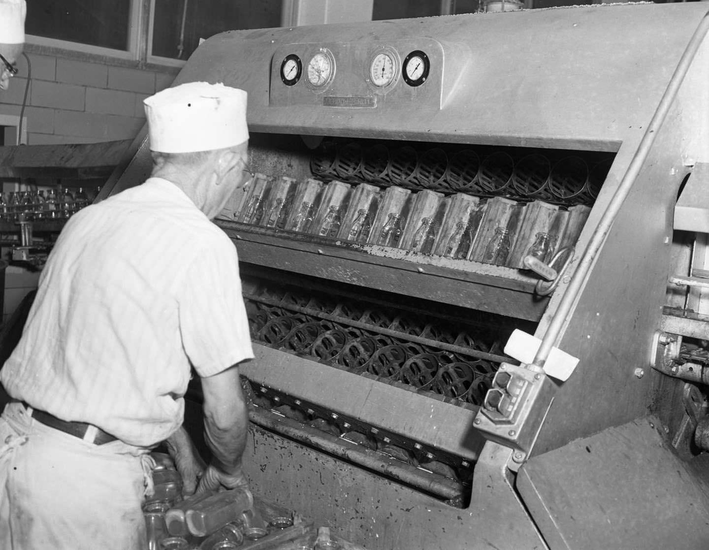 A machine at a dairy in Abilene, 1958. Fourteenth and Butternut Streets. A worker is putting glass bottles into the machine.
