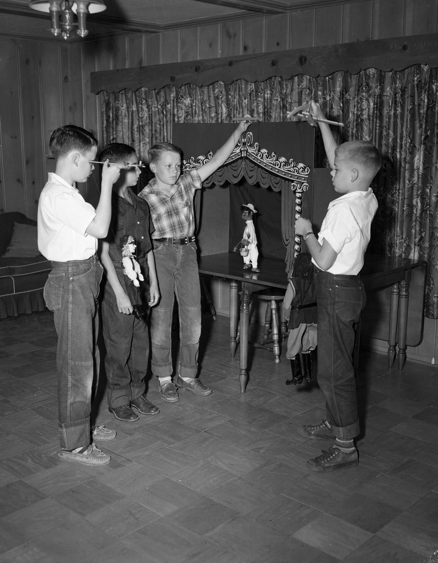 Four young boys playing with puppets, 1958. By the children there is a table with what seems to be a puppet theater box on it.