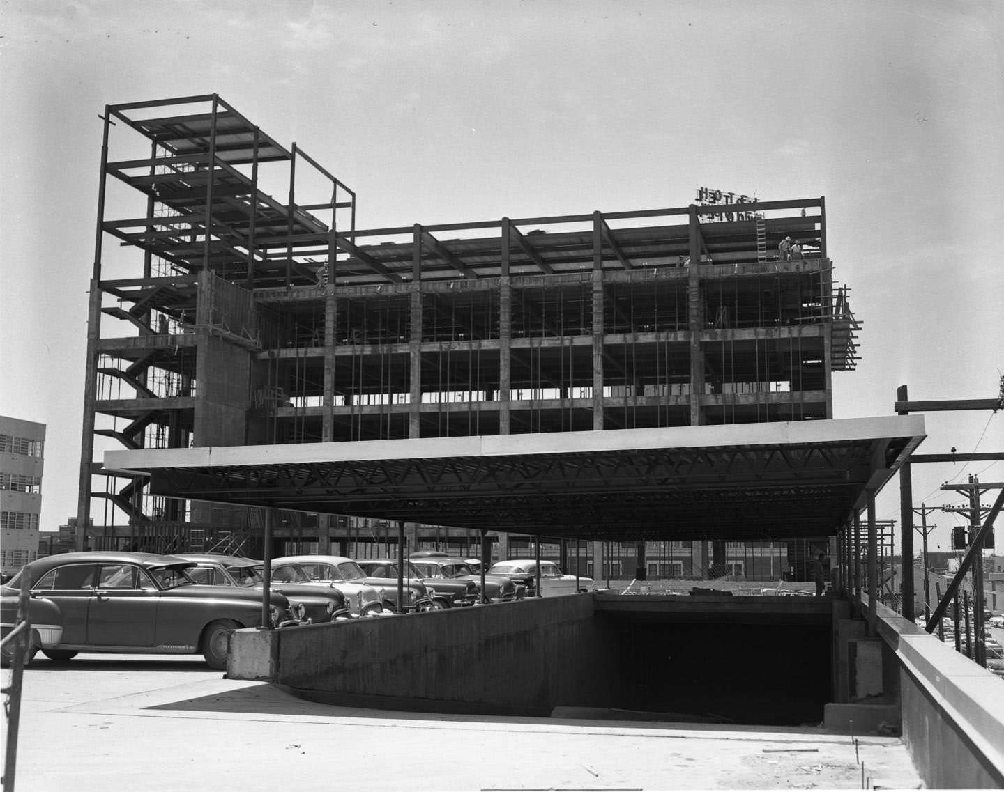 The Citizens National Bank under construction, 1954. The multi-story building's frame is partially completed. There are men working and cars parked at the site.